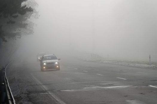 Cars in the fog. Bad winter weather and dangerous automobile traffic on the road. Light vehicles in fog.