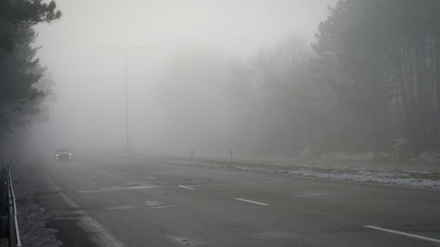 Cars in the fog. Bad winter weather and dangerous automobile traffic on the road. Light vehicles in fog.