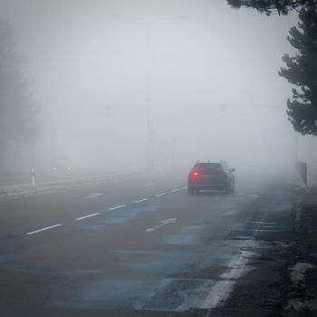 Bad weather driving - foggy hazy country road. Motorway - road traffic. Winter time.