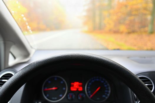 Car interior with dashboard on wet road in autumn season. Foggy and dangerous driving - concept for traffic and road safety - view from the driver's seat.