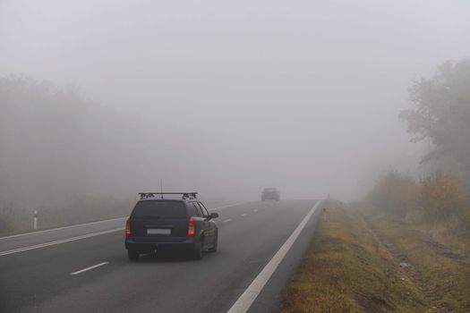 Car on the road in the fog. Autumn landscape - dangerous road traffic in winter season.