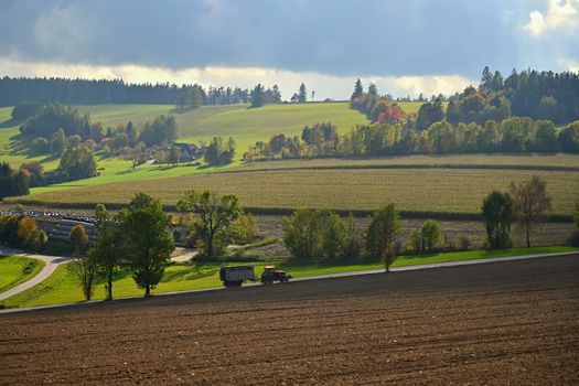 Tractor on the field. Beautiful autumn nature with landscape in the Czech Republic. Colorful trees with blue sky and sun. Background for autumn and agriculture.