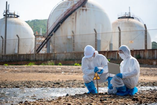 Biologist wear protective suit and mask collects sample of waste water from industry, problem environment, Ecologist sample taken dead fish to inspection and save data to laptop computer, Toxic water