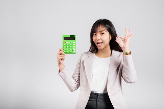 Tax day concept. Woman confident smiling holding electronic calculator and show OK gesture, excited happy Asian female studio shot isolated on white background, Account and finance counting income