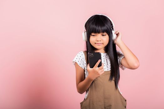 Asian kid 10 years enjoying listening music from mobile phone wear wireless headset at studio shot isolated on pink background, Happy child girl lifestyle use smartphone listen music with headphones