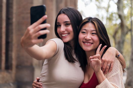 two young women smiling and having fun taking a selfie photo with a cell phone, concept of friendship and technology of communication