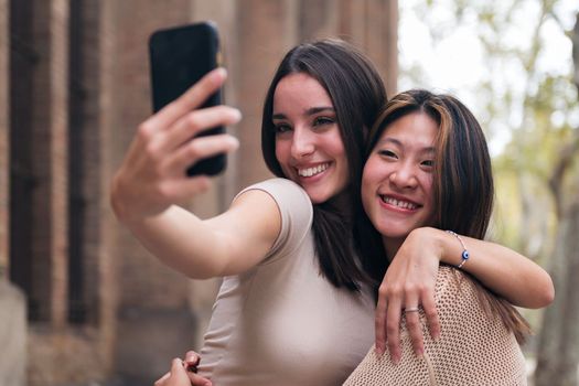 two young women smiling and having fun taking a selfie photo with a cell phone, concept of friendship and technology of communication