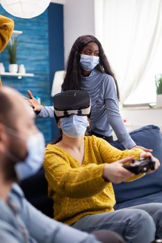 Woman playing video games experiencing virtual reality wearing vr headset, face mask to prevent coronavirus spread keeping social distancing , spending time withl multi ethnic friends . New normal party.