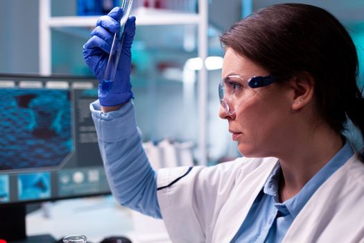 Close up of scinetist analyzing liquid medical test tube in scientific lab. Pharmaceutical biotechnologist in research laboratory works with test tube to find vaccine glove.