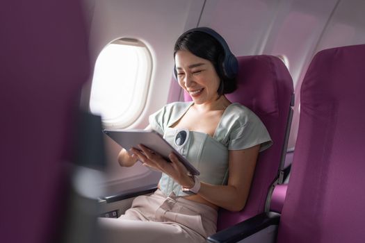 Joyful asian woman sits in the airplane and using tablet while go to travel.