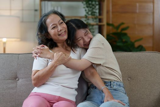 Happy senior Asian woman and her adult daughter are cuddling on the couch.