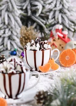 Hot chocolate with marshmallows in a white ceramic mug, with tangerines on a snowy table. The concept of a cozy holiday for Christmas and New Year.