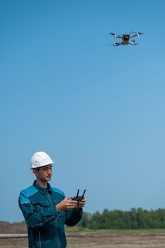 A man in a helmet and overalls controls a drone at a construction site. The builder carries out technical oversight