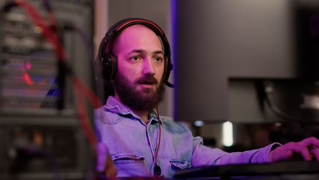 Handheld shot of gamer with headset streaming gameplay shouting after winning online multiplayer game on gaming pc setup. Caucasian man celebrating victory in online computer competition with friends.