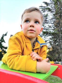 Adorable little toddler boy having fun on playground, child wearing yellow hoody jacket. High quality photo