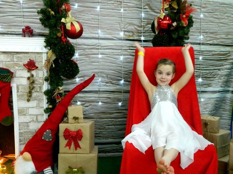 A little girl in holds a box of gifts and rejoices. The child sits near a Christmas tree and unpacks gifts. High quality photo