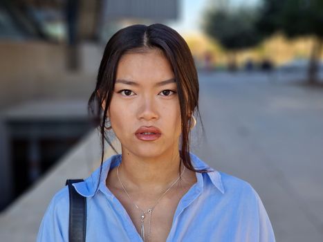 Chinese girl looking at camera with a serious expression in urban background. Female wearing casual clothes.