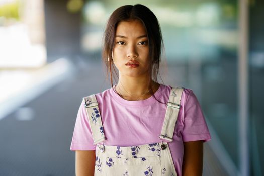 Young Chinese woman looking at camera with serious expression in a modern office building. Female wearing casual clothes.
