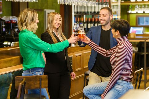 Happy multiethnic adult people in casual clothes smiling and clinking glasses of alcohol drinks while resting near counter in weekend in bar