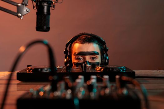 Disc jockey looking closely at turntables in studio, acting silly and being focused on mixer to produce music. Feeling playful and serious about mixing techno sounds, audio equipment.