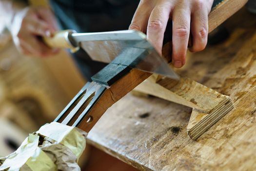 Crop male artisan using sharp knife to cut wood, marking the frets on neck of Spanish flamenco guitar during work in professional luthier workshop
