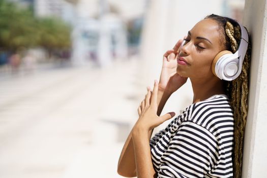 Beautiful young black female listening to music with wireless headphones outdoors.