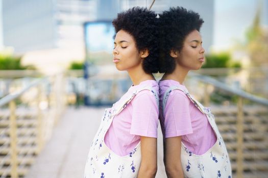 Side view of African American female with closed eyes standing near glass building on street of city against blurred background