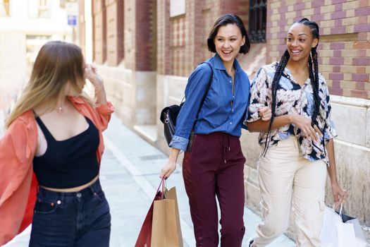 Cheerful young multiracial female millennials smiling happily while walking in city and chatting after successful shopping