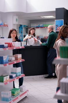 Senior customer standing at drugstore counter buying cardiology pills during medical consultation. Pharmacist helping client with supplements recommandation. Health care service support