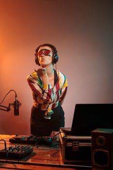Female musician blowing air kisses in studio, being romantic and acting flirty while she mixes techno music at turntables. Charming dreamy artist trying to remix song at electric mixer.