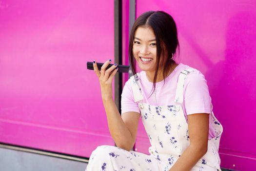 Cheerful Asian young woman using recording a voice note in her smartphone. Chinese female wearing casual clothes.