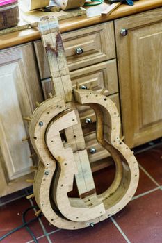 From above wooden mould for making Spanish flamenco guitar placed on tiled wall near cabinets in professional luthier workshop.