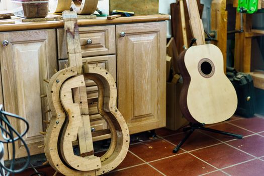 From above wooden mould for making Spanish flamenco guitar, next to unfinished guitar, placed on tiled wall near cabinets in professional luthier workshop.