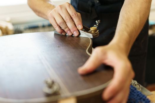 Crop craftsman using plane to shave traditional Spanish flamenco guitar on workbench in workshop