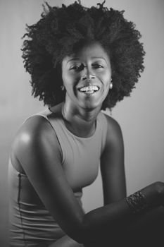 Happy African American woman with curly hair smiling and looking at camera under violet neon light. Black and white photograph.