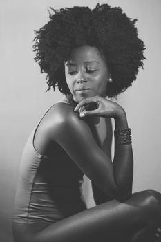 Side view of black woman in bodysuit with Afro hairstyle touching chin and looking away over shoulder while sitting under. Black and white photograph.