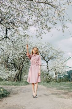Blonde girl on a spring walk in the garden with cherry blossoms. Female portrait, close-up. A girl in a pink polka dot dress