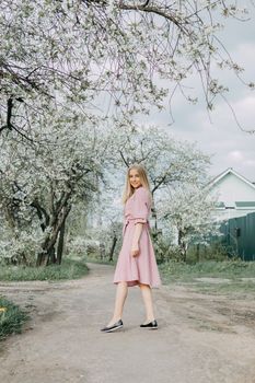Blonde girl on a spring walk in the garden with cherry blossoms. Female portrait, close-up. A girl in a pink polka dot dress