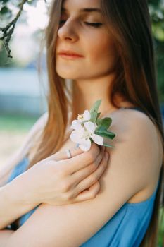 Beautiful young girl in a blue dress in a blooming Apple orchard. Blooming Apple trees with white flowers. Portrait of a woman in the bloom of the Apple trees.
