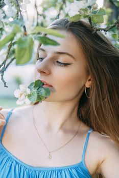 Beautiful young girl in a blue dress in a blooming Apple orchard. Blooming Apple trees with white flowers. Portrait of a woman in the bloom of the Apple trees.