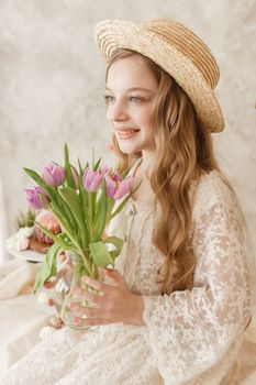 A girl with long hair in a dress and hat is sitting at the Easter table with cakes, spring flowers and quail eggs. Happy Easter celebration
