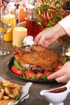 Woman serving baked drumstick turkey on a tray of vegetables on the dining table.. Happy Thanksgiving.