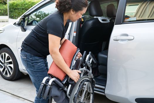 Asian woman folding and lift up wheelchair into her car. Accessibility concept.