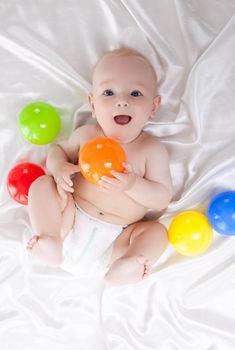 Portrait of happy baby lying in bed with colored balls. Top view