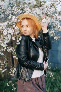 Portrait of a woman in a straw hat in a cherry blossom. Free outdoor recreation, spring blooming garden.