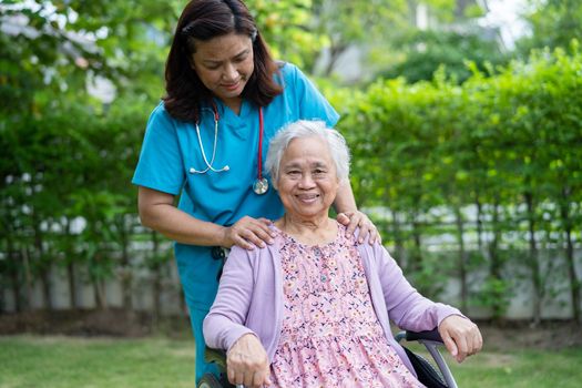 Doctor caregiver help and care Asian senior or elderly old lady woman patient sitting on wheelchair in park at nursing hospital, healthy strong medical concept