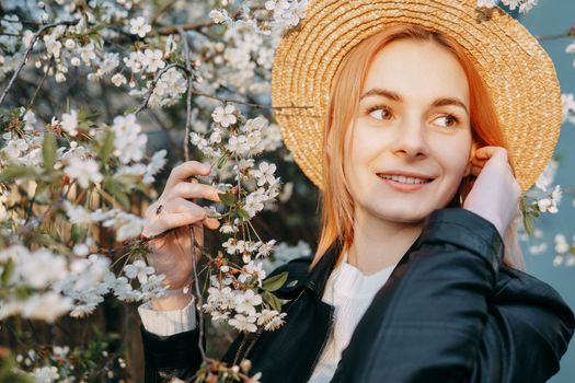Portrait of a woman in a straw hat in a cherry blossom. Free outdoor recreation, spring blooming garden