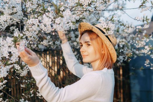 Portrait of a woman in a straw hat in a cherry blossom. Free outdoor recreation, spring blooming garden