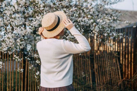 Portrait of a woman in a straw hat in a cherry blossom. Free outdoor recreation, spring blooming garden