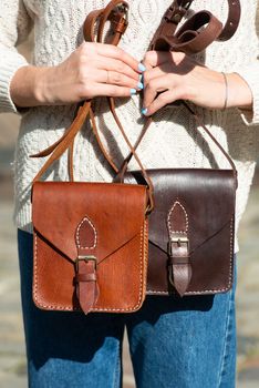 close-up photo of two brown messanger leather bag in womans hands . outdoors photo